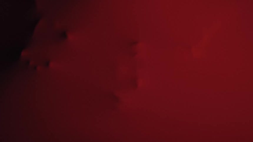 A smooth red fabric surface shows several small protrusions pressing from beneath in a dark minimalist scene
