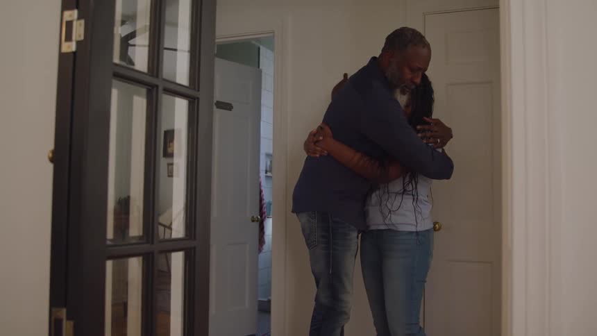 A young father hugged his teenage daughter consoling her as she looks sad standing beside the door while indoor midday