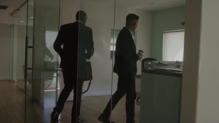 Two adults interact in modern office with glass walls and natural lighting