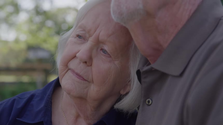 Elderly couple shares a tender moment outdoors with affectionate gesture and serene expression