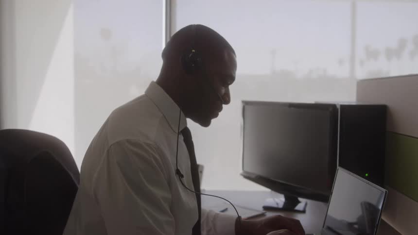 Person seated at office desk with two monitors laptop smartphone glasses coffee and documents