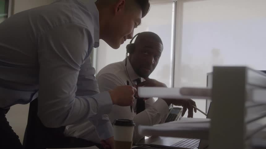 Coworkers reference a computer during a conversation in the office
