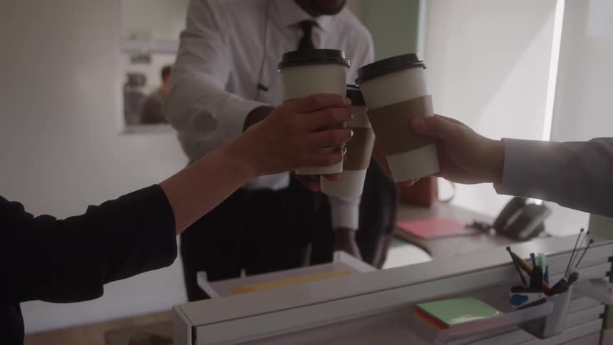 Three people in an office toasting with coffee cups