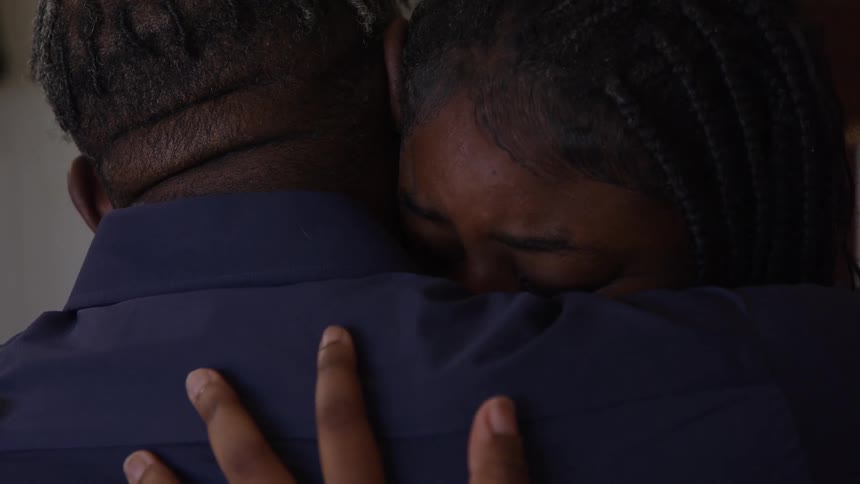 The video is a closeup shot of an african american man and a young woman with braids showing a tender interaction the mans arm is visible as he pulls the woman into an embrace and the woman looks upset or tearful before resting her head on his should