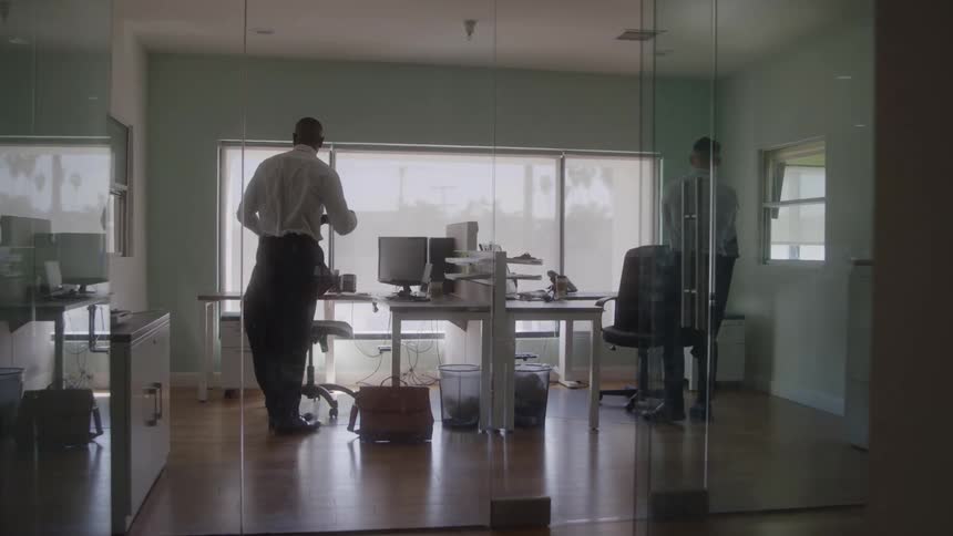 Two men take off their jackets and prepare to work in a glass walled office