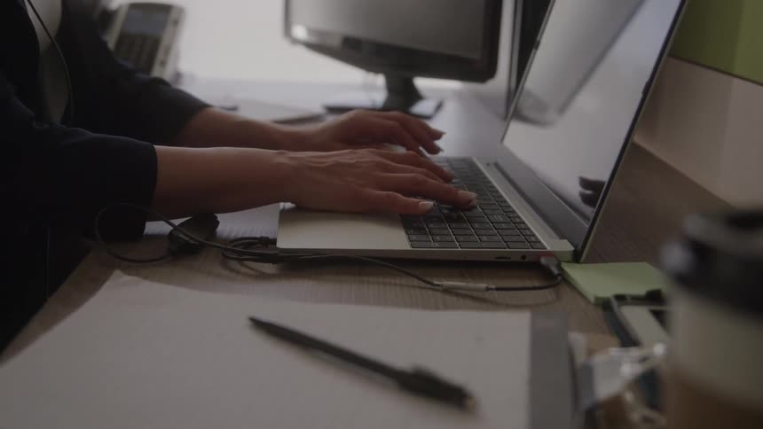 Closeup of hands typing on a laptop at a cluttered office desk