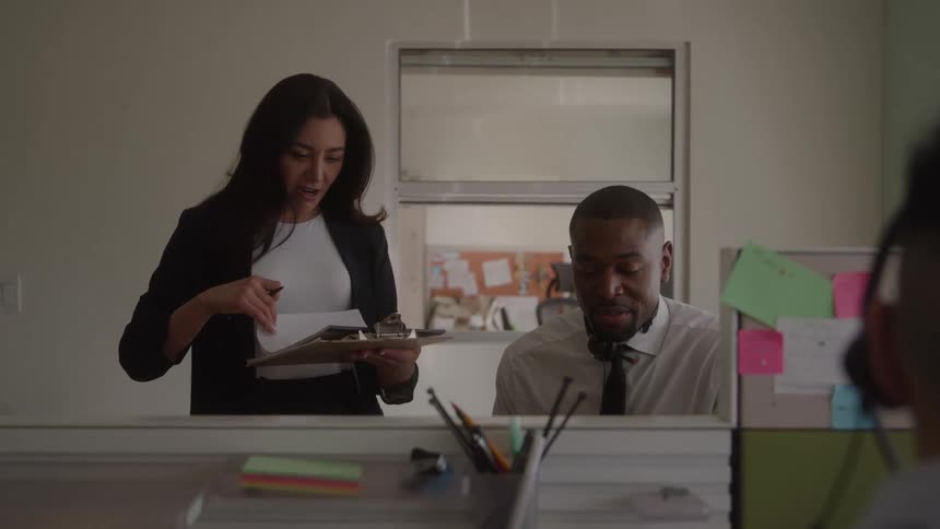 Two coworkers smile and discuss work together in an office cubicle