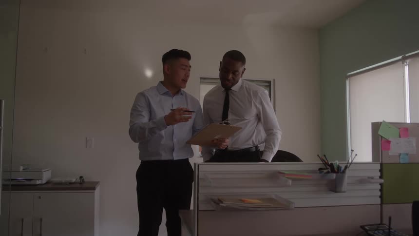 Colleagues discuss documents on a clipboard inside a welllit office