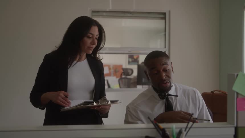 Two coworkers review documents together at a desk in an office