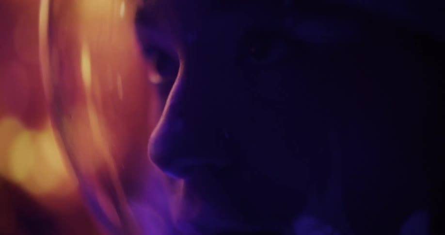 An astronauts face is seen in profile inside their helmet illuminated by colorful flashing lights
