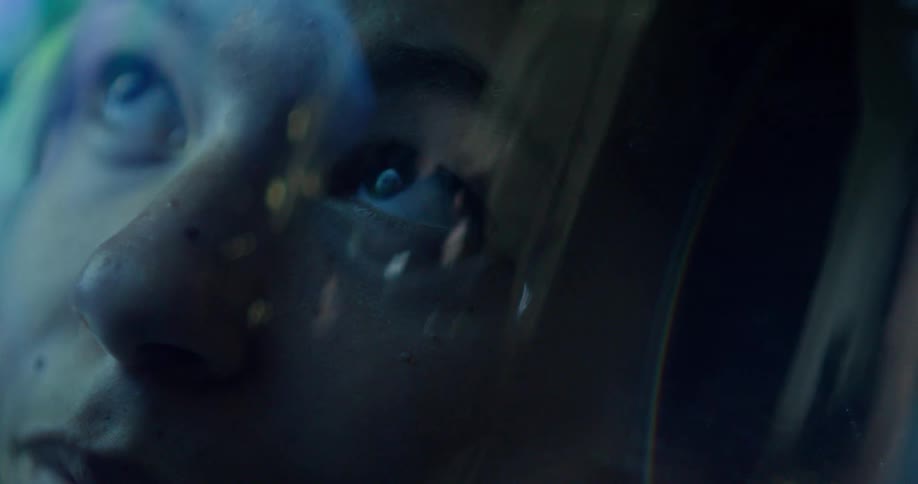 An astronauts awe filled eyes look up from inside their helmet as colorful cosmic lights reflect off thier visor