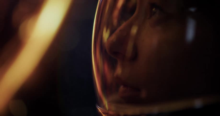 A closeup of a person wearing a astronaut visor with warm light reflections