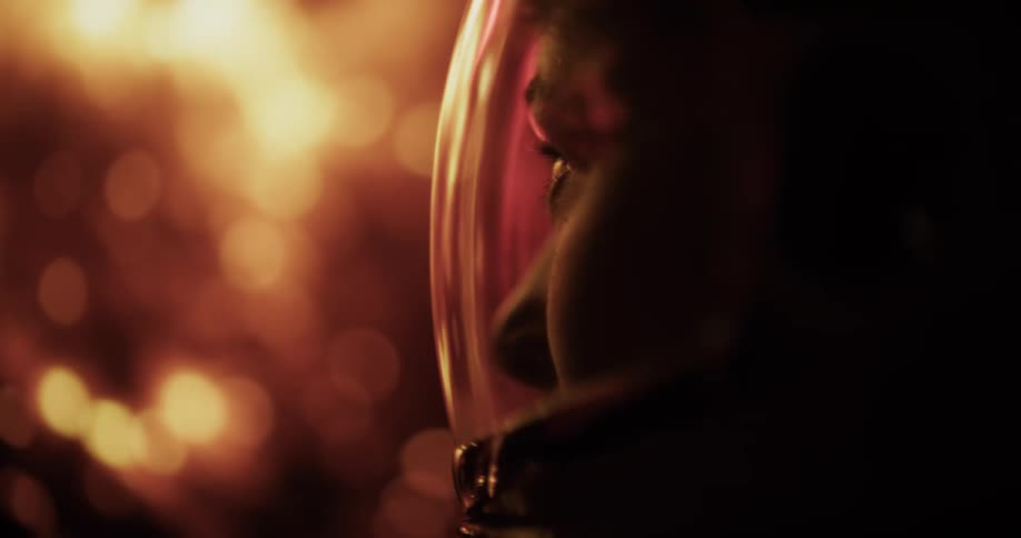 The video is a closeup profile shot of an individuals face inside a reflective helmet or visor the scene is dark with warm orange light reflecting on the edge of the helmet suggesting a lowlight or futuristic environment