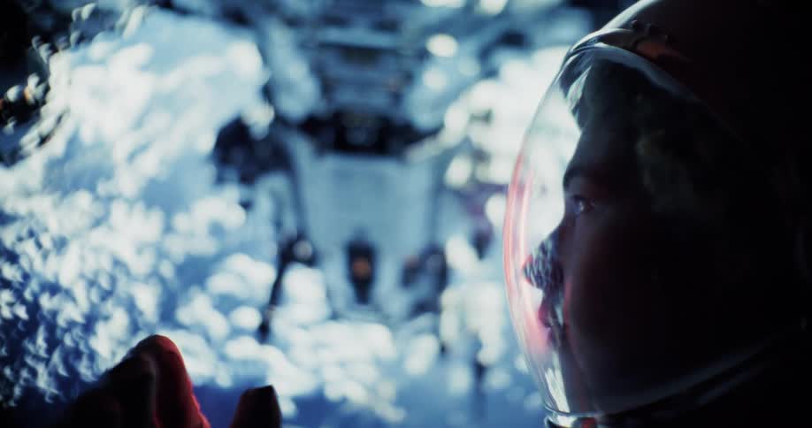 A person in a space helmet gazes out at the blurred glowing interior of a spacecraft