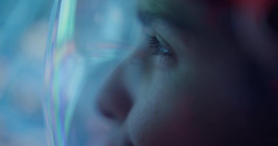 Closeup of an astronaut wearing a helmet visor illuminated by cool blue futuristic light
