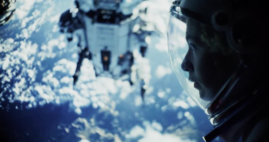 A close profile view shows a womans face in a space helmet looking down at a large spaceship and the blue and white clouds of earth far below