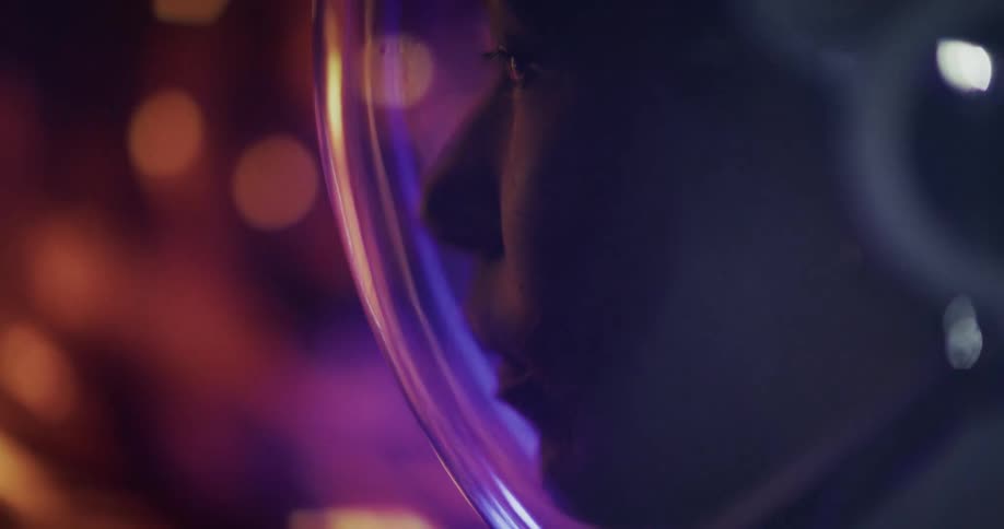 A closeup of a person wearing a futuristic helmet lit by colorful reflections