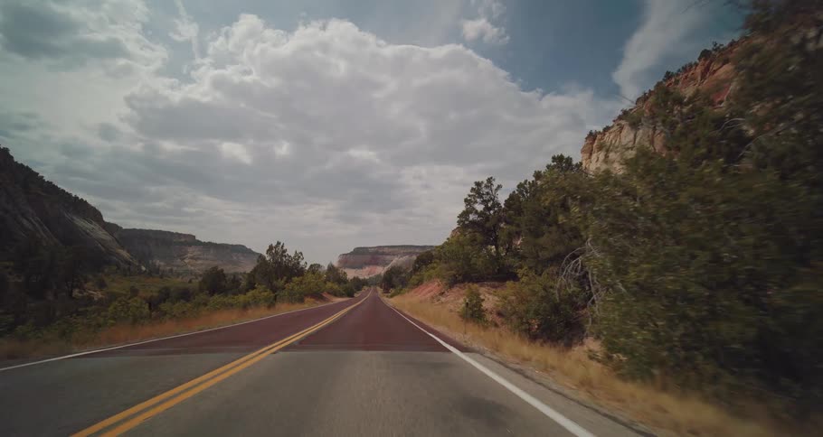 Straight road surrounded by cliffs and vegetation under a cloudy sky
