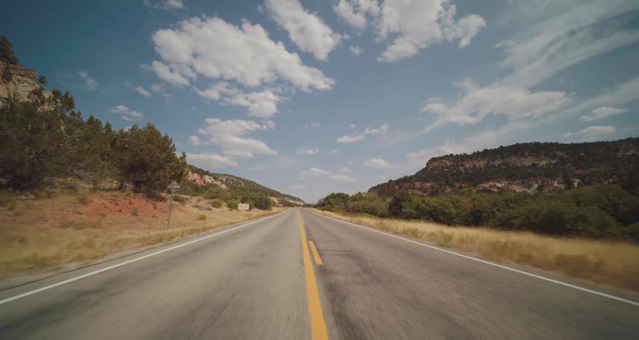 An empty road stretches toward distant hills under a vast partly cloudy sky