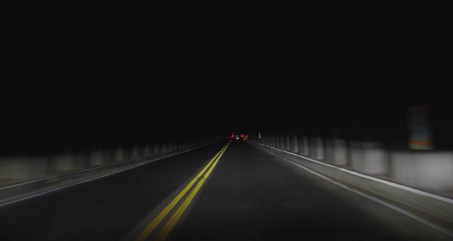 A cars headlights illuminate the road as it follows another vehicle through a tunnel at night