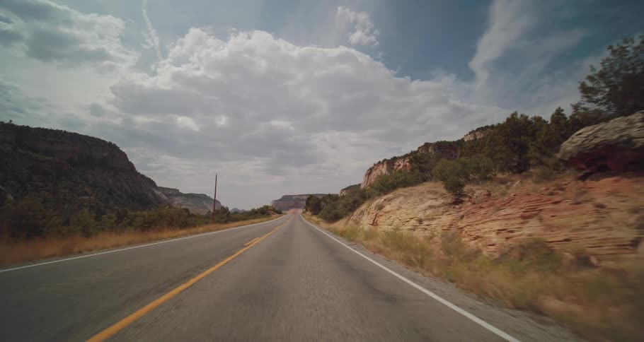 A highway road winds through a canyon between mountains under a cloudy sky