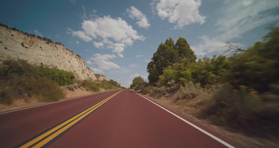 A road winds through a canyon with rocky cliffs and trees under a cloudy sky