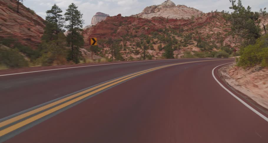Winding road cuts through a canyon of reddish rocks and sparse vegetation