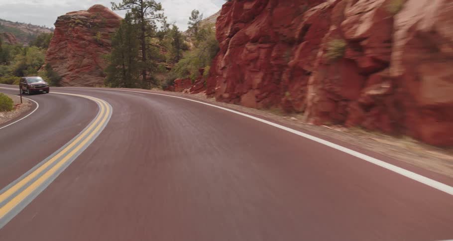 Car drives along a curve surrounded by reddish rocks