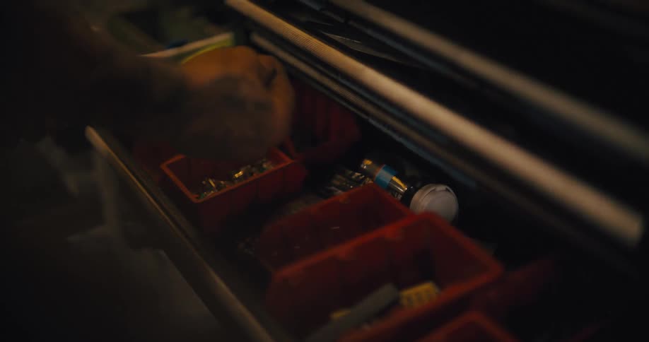 Hand selects small parts in a workshop drawer lit by warm light