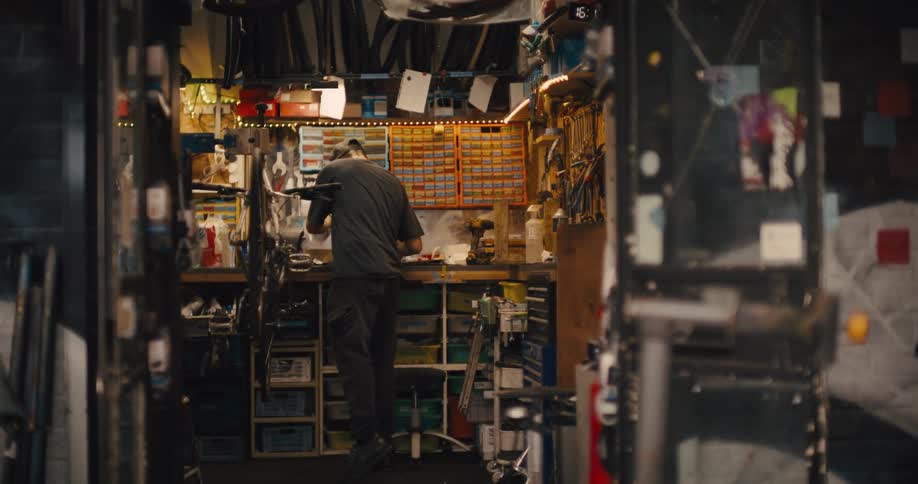 Hand held medium wide shot of a  mechanic in a cluttered bicycle workshop