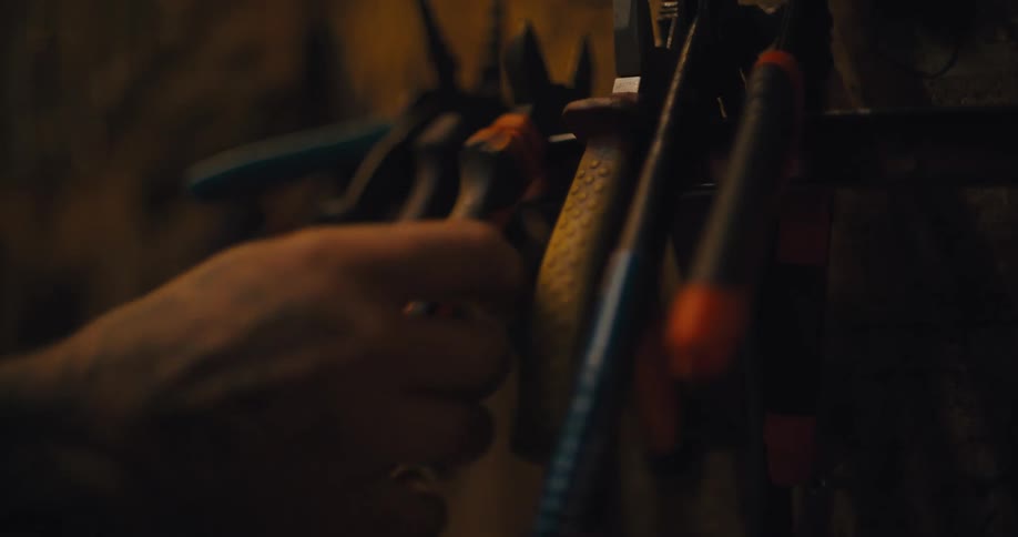 Hand hesitating before choosing a set of pliers  tools hanging on a workshop wall