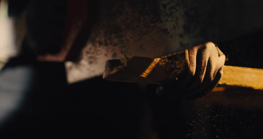 A gloved hand grips a piece of wood as a saw cuts through it