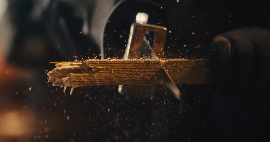 An electric saw cuts through wood under warm light producing small flecks of sawdust