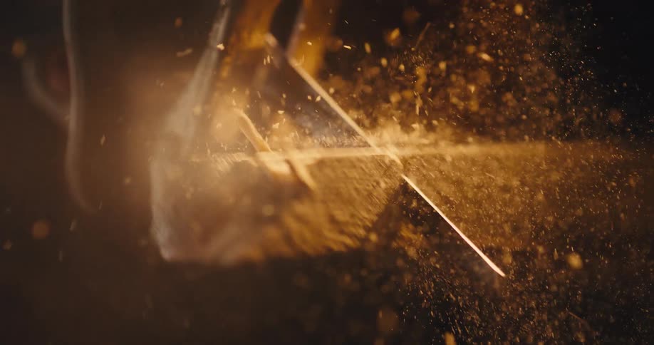 Light flares into the lens as a mechanical saw cuts through wood sending sawdust into the air