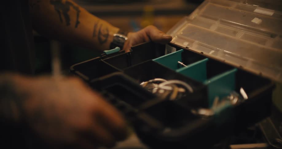 A man is looking through a plastic box of hardware in a workshop