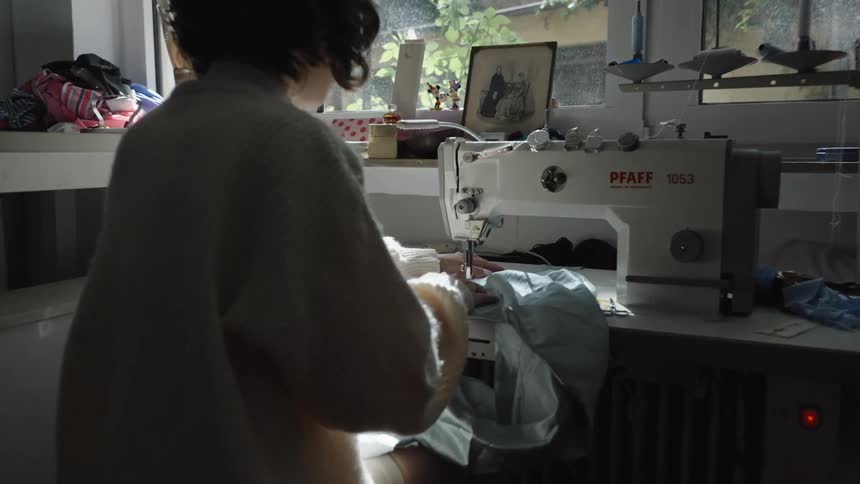 Person sews blue fabric on an industrial sewing machine near a sunlit window