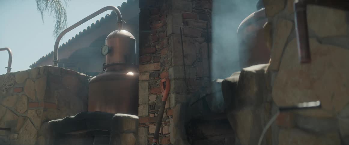 Copper distillation equipment releasing steam beside a stone wall