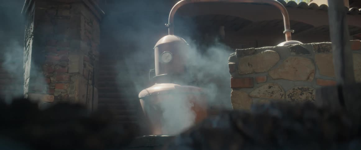 Copper distillation equipment emitting steam between brick and stone walls