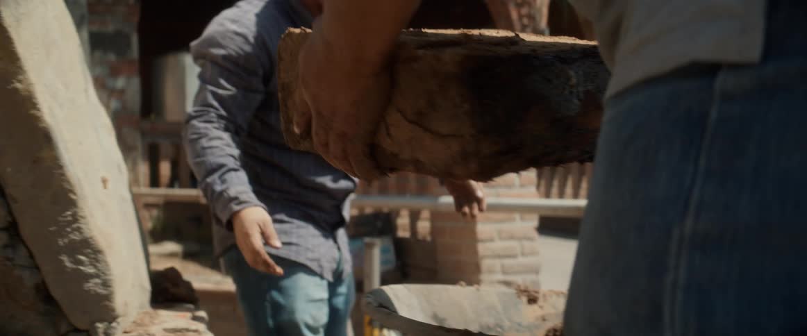 Workers move clay blocks beside a wheelbarrow