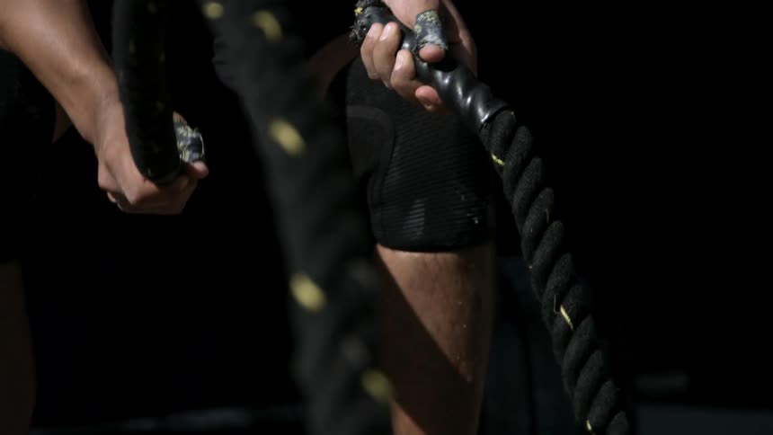 A muscular person grips battle ropes during an intense workout in a gym