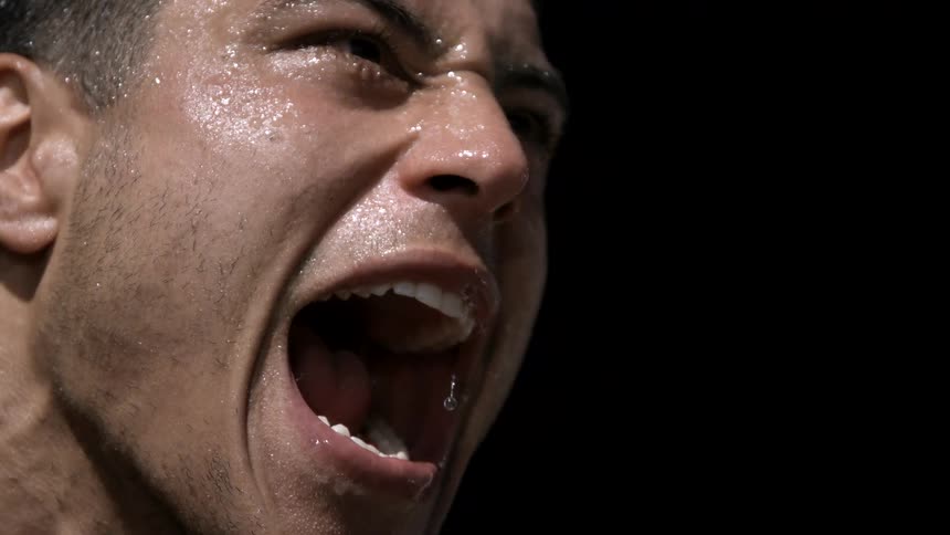A young black man inside a dark room screams with a sweaty face