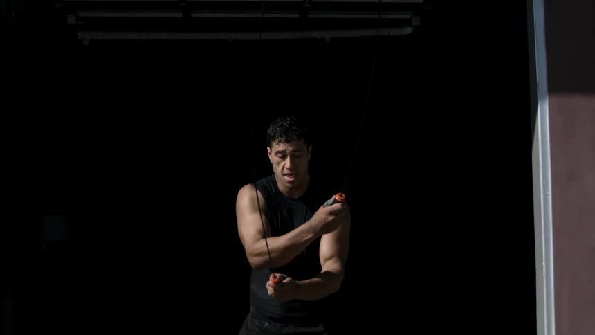 A muscular young man exercises with a jump rope against a dark background