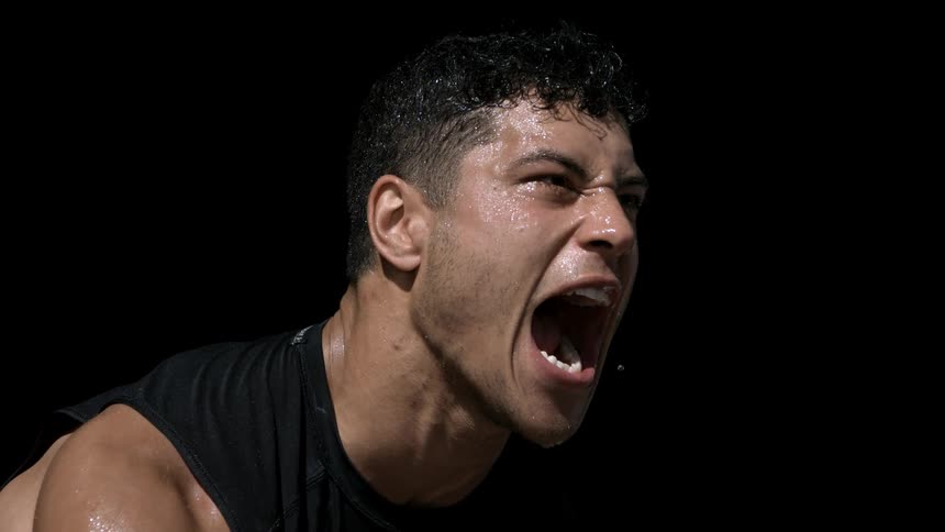 A closeup of a sweating man shouting with intensity against a black background