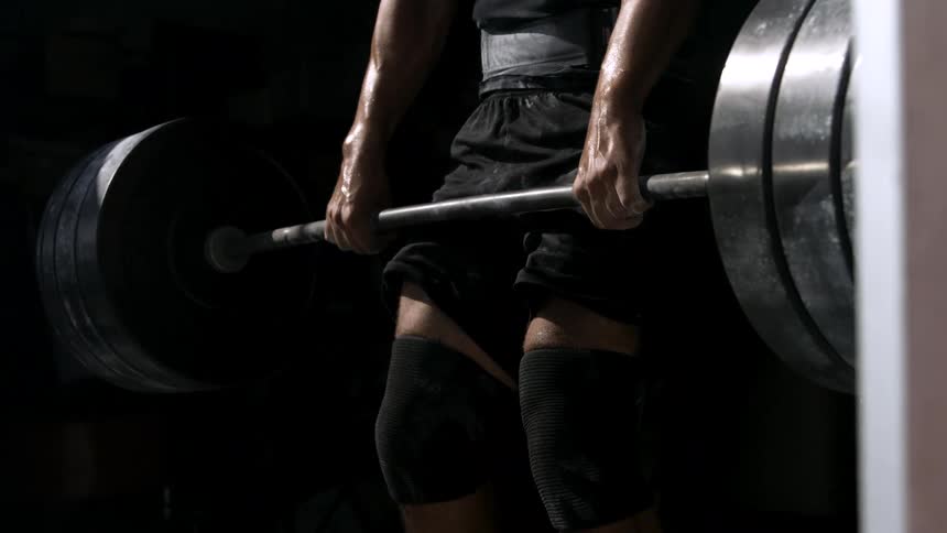 A muscular man lifts a heavy barbell with intense focus in a dark gym