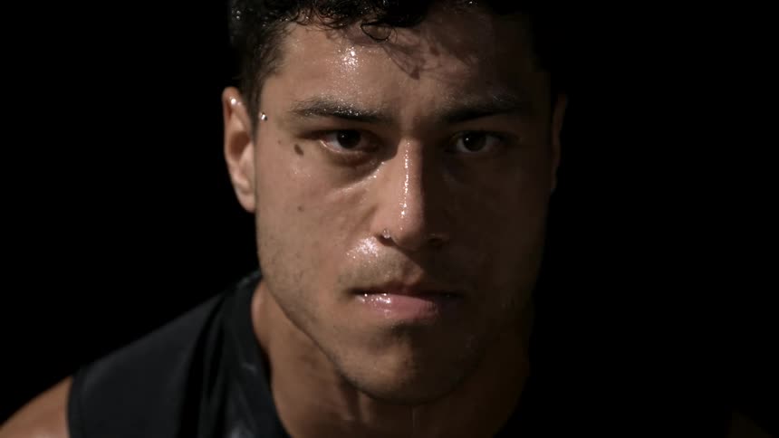 A sweaty man stares forward with intense focus against a black background