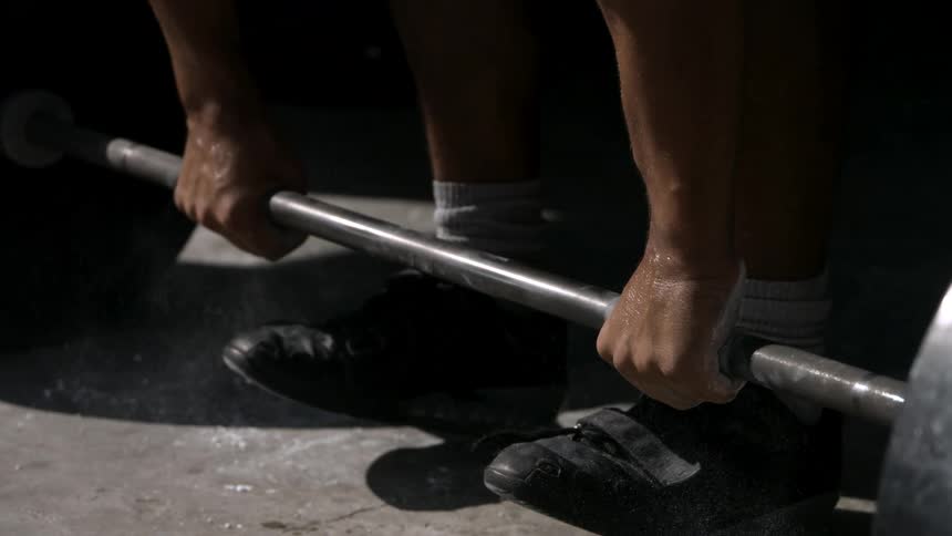 A man in the gym rubs white chalk on his palms before lifting a weight