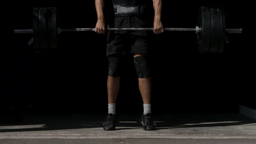 A man braces to deadlift a heavily loaded barbell muscles tensed in a pool of light against a dark backdrop
