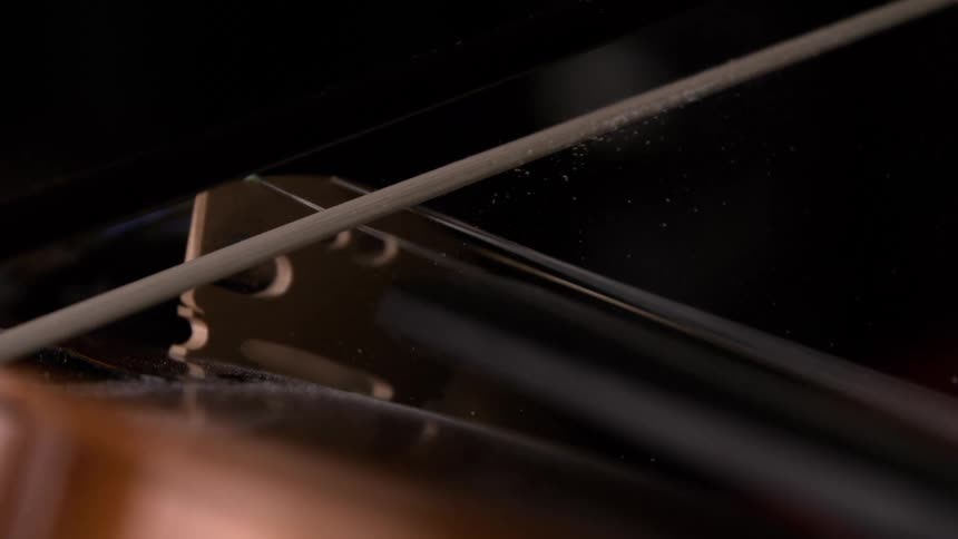 A violin bow glides across the strings near the bridge in a tight closeup