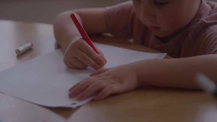 Young boy sitting at a table drawing on paper