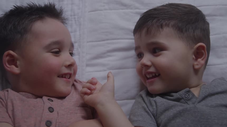 Twin boy infants are smiling as one puts his finger on the other ones face